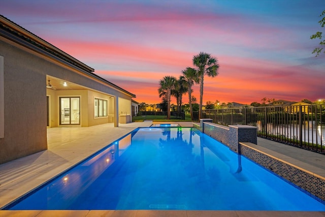 pool at dusk featuring an in ground hot tub, a patio, and a water view