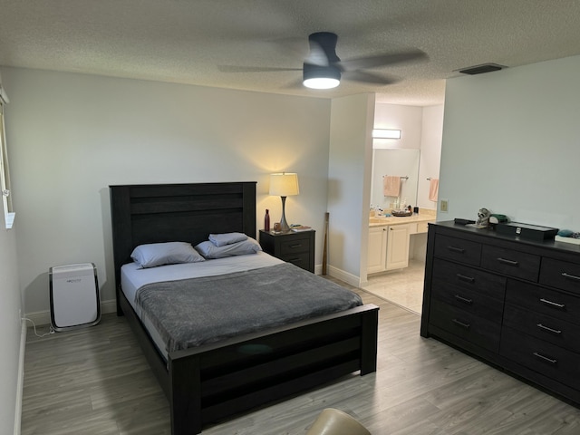 bedroom with a textured ceiling, ceiling fan, light hardwood / wood-style flooring, and ensuite bath