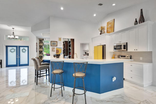 kitchen with decorative backsplash, stainless steel appliances, a large island with sink, white cabinets, and a breakfast bar area