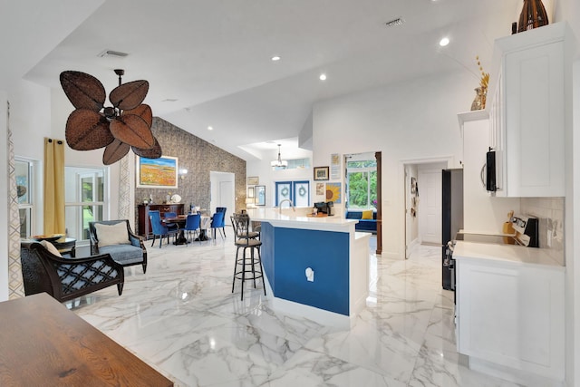 kitchen featuring high vaulted ceiling, white cabinets, ceiling fan, a kitchen bar, and kitchen peninsula