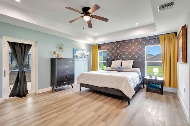 bedroom featuring ceiling fan, a raised ceiling, and light wood-type flooring