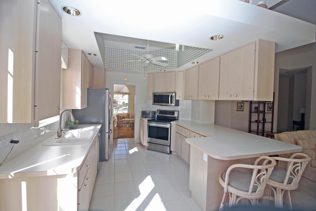 kitchen with sink, kitchen peninsula, a kitchen bar, light tile patterned floors, and appliances with stainless steel finishes