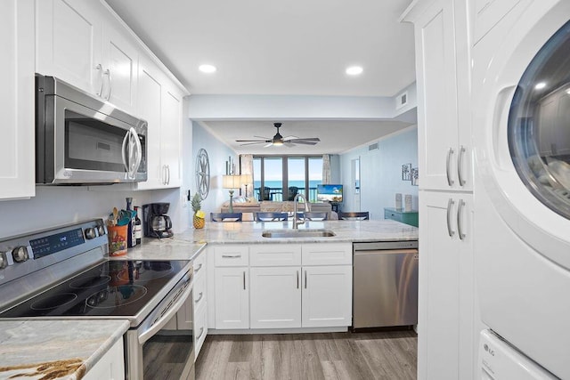 kitchen with kitchen peninsula, stainless steel appliances, sink, stacked washer / dryer, and white cabinetry