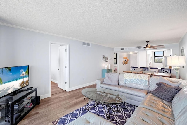 living room featuring ceiling fan, wood-type flooring, a textured ceiling, and ornamental molding