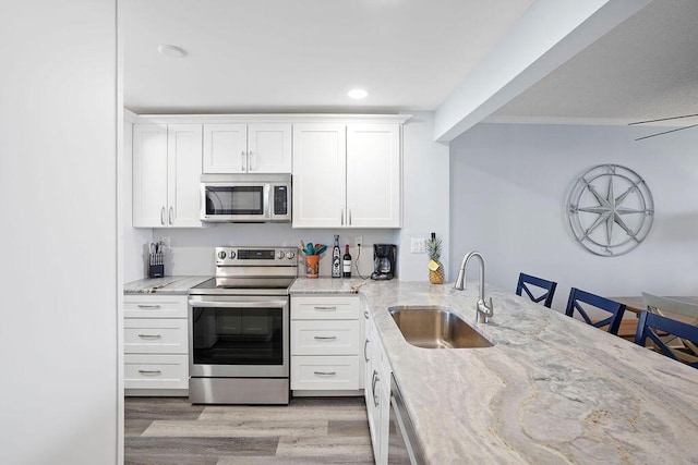 kitchen featuring white cabinetry, sink, light stone counters, and appliances with stainless steel finishes