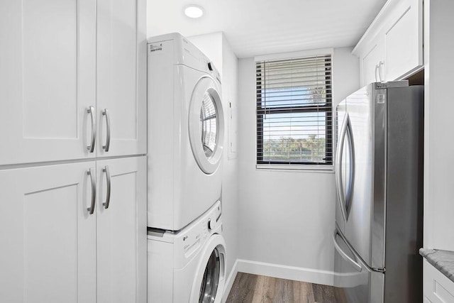 laundry room featuring stacked washing maching and dryer, cabinets, and wood-type flooring