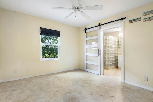 empty room featuring light tile patterned flooring, ceiling fan, and a barn door