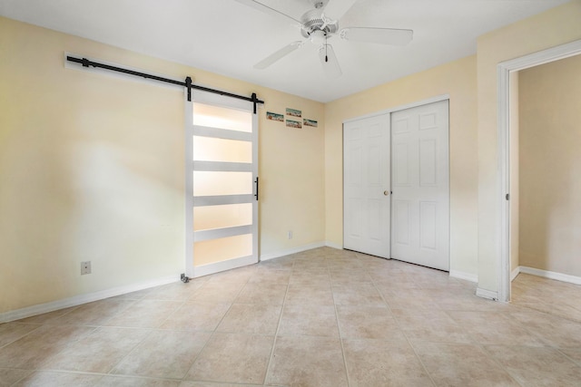 unfurnished bedroom featuring a barn door, light tile patterned floors, ceiling fan, and a closet