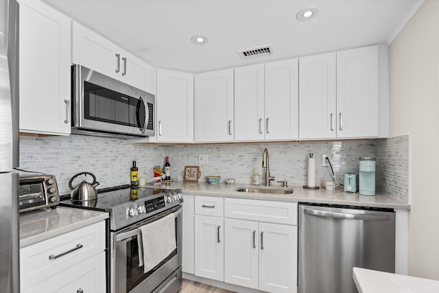 kitchen featuring visible vents, backsplash, appliances with stainless steel finishes, white cabinetry, and a sink