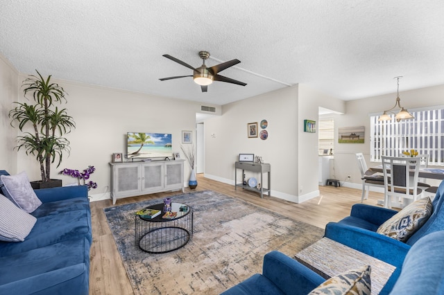 living room featuring a textured ceiling, ceiling fan, wood finished floors, visible vents, and baseboards