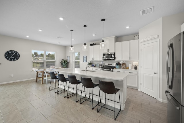 kitchen with a kitchen island with sink, white cabinets, sink, decorative light fixtures, and stainless steel appliances