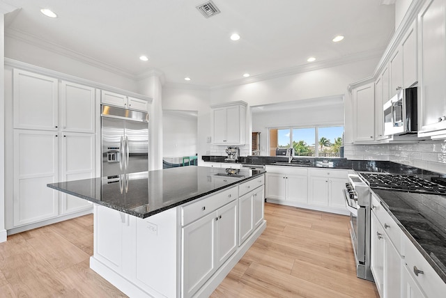 kitchen with white cabinets, a center island, high end appliances, and dark stone counters