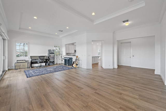 unfurnished living room featuring light wood-type flooring, a raised ceiling, and ornamental molding