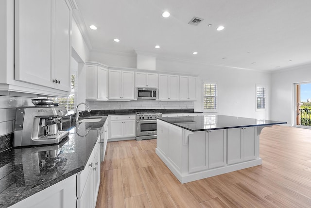 kitchen with dark stone counters, a breakfast bar, stainless steel appliances, sink, and white cabinetry