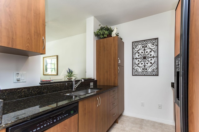 kitchen featuring dishwashing machine, dark stone countertops, light tile patterned floors, and sink