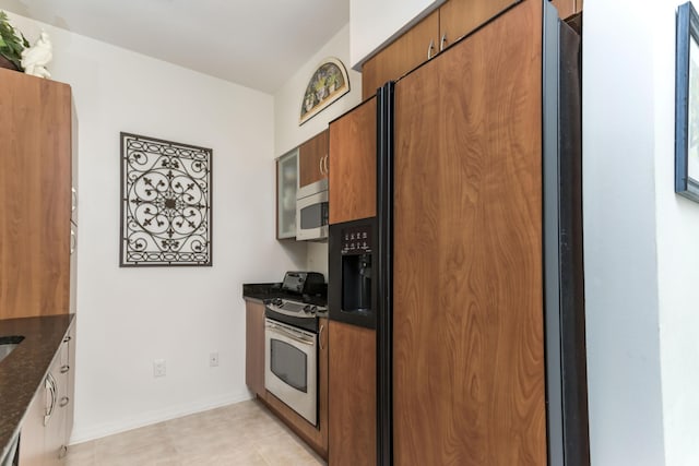 kitchen featuring stainless steel stove, dark stone countertops, high end fridge, and brown cabinets