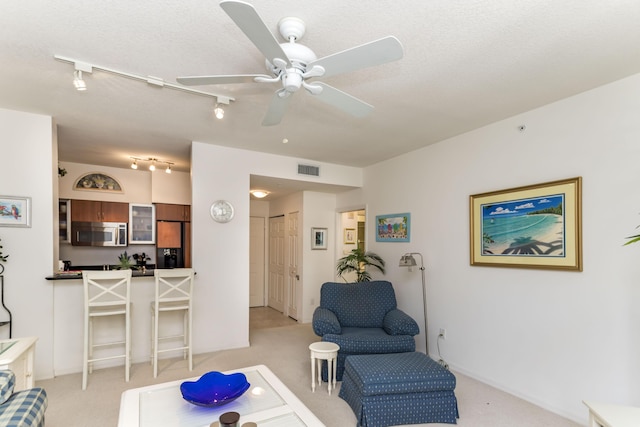 living area featuring a ceiling fan, rail lighting, light colored carpet, and visible vents