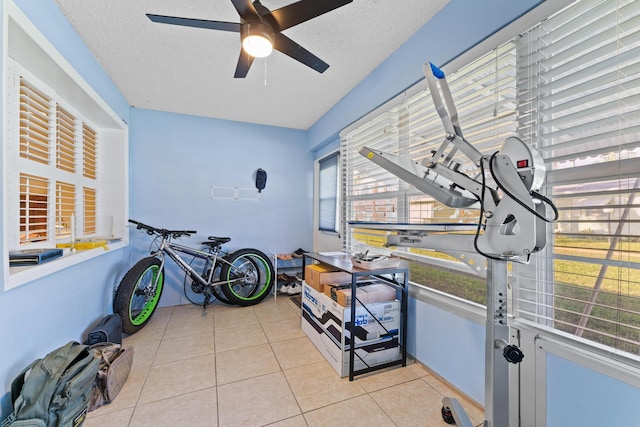 workout area featuring ceiling fan, light tile patterned floors, and a textured ceiling