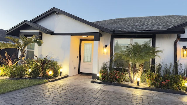 property entrance featuring a shingled roof and stucco siding