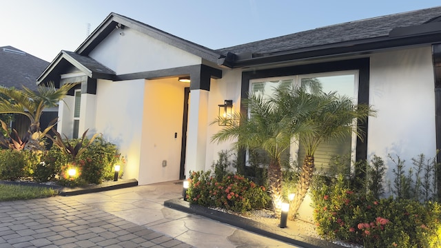 view of exterior entry featuring roof with shingles and stucco siding