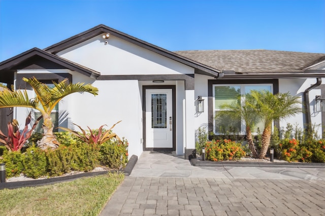 property entrance with roof with shingles and stucco siding