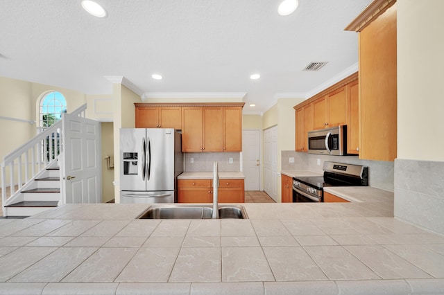 kitchen with tile counters, sink, stainless steel appliances, backsplash, and ornamental molding