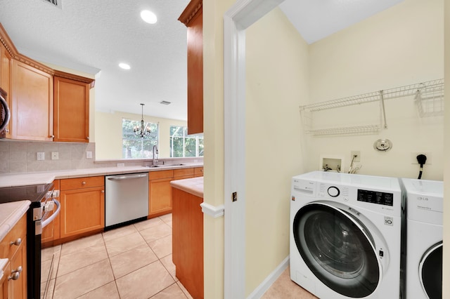 clothes washing area with washer and clothes dryer, sink, a textured ceiling, light tile patterned flooring, and a chandelier