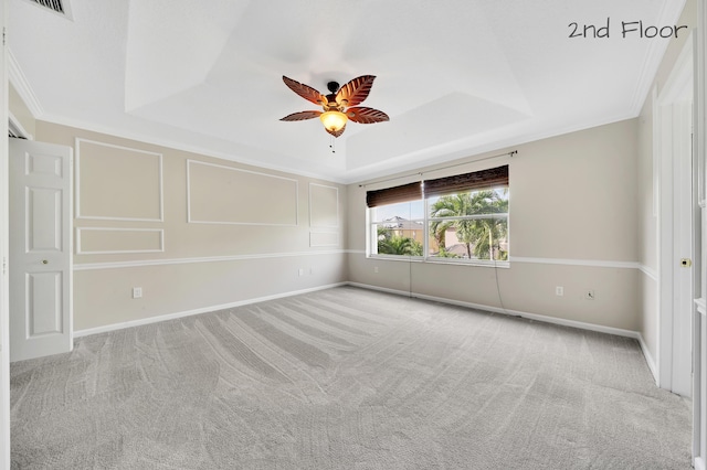 carpeted spare room with a tray ceiling, ceiling fan, and ornamental molding