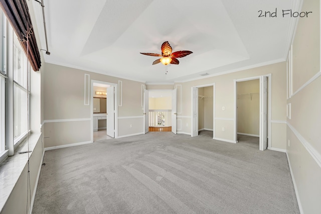 unfurnished bedroom with ceiling fan, a raised ceiling, light colored carpet, and connected bathroom