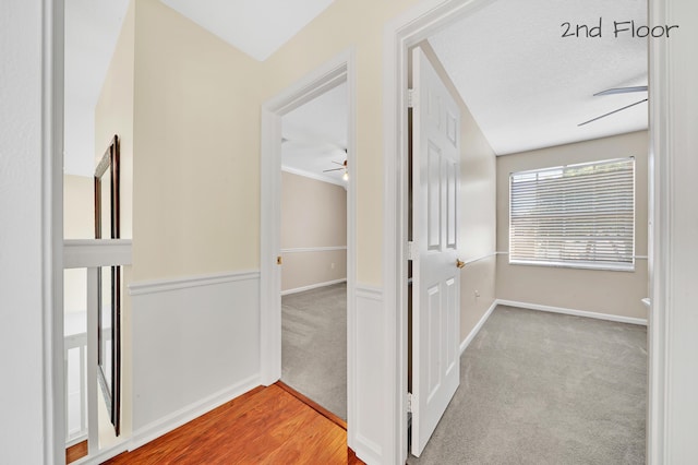 hallway with light carpet, a textured ceiling, and ornamental molding