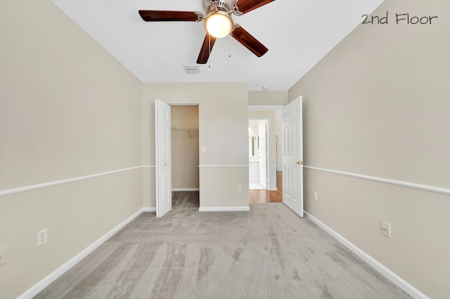 unfurnished bedroom featuring ceiling fan, a spacious closet, light carpet, and a closet