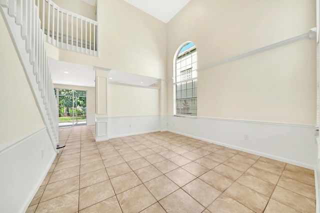 empty room with a towering ceiling, light tile patterned floors, and decorative columns