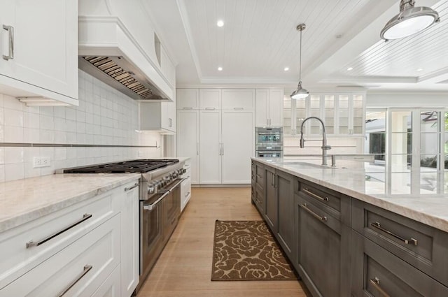 kitchen featuring white cabinetry, sink, stainless steel appliances, light stone counters, and custom range hood