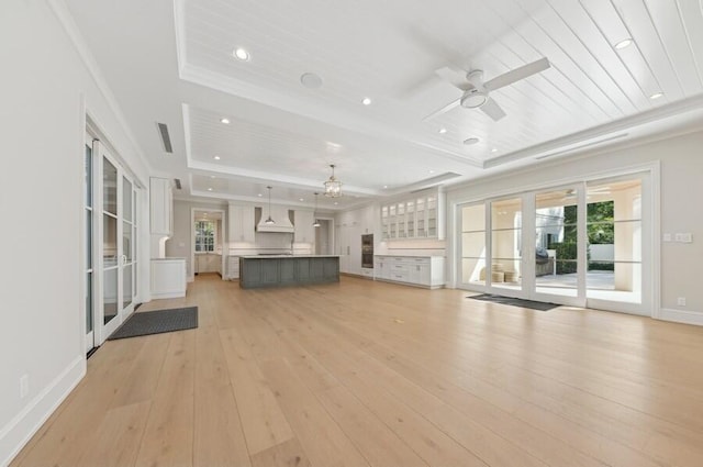 unfurnished living room featuring ceiling fan, wooden ceiling, a raised ceiling, light wood-type flooring, and ornamental molding