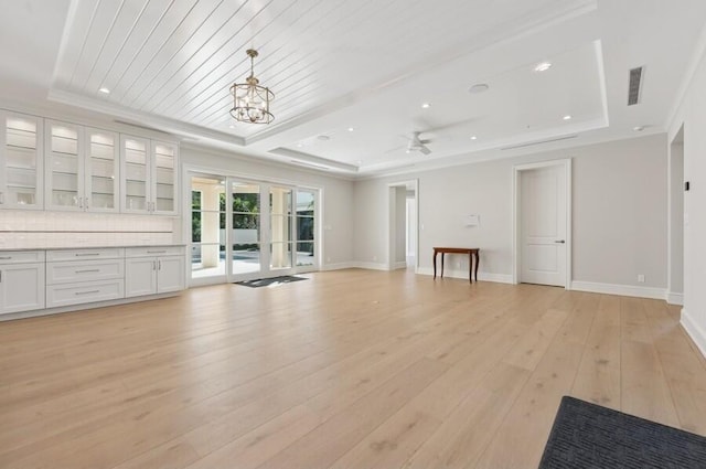 unfurnished living room with ceiling fan with notable chandelier, a raised ceiling, and light wood-type flooring