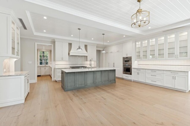 kitchen featuring pendant lighting, premium range hood, white cabinetry, and a kitchen island with sink