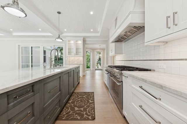 kitchen with high end stove, custom range hood, light wood-type flooring, light stone counters, and white cabinetry