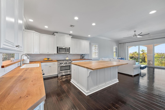 kitchen with appliances with stainless steel finishes, sink, white cabinets, a kitchen island, and butcher block counters