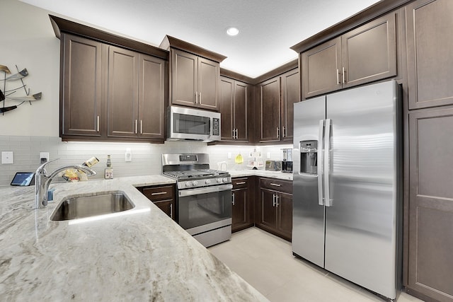 kitchen with decorative backsplash, appliances with stainless steel finishes, light stone counters, dark brown cabinets, and sink