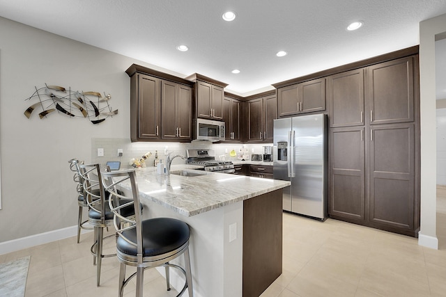 kitchen featuring sink, stainless steel appliances, light stone counters, kitchen peninsula, and dark brown cabinets