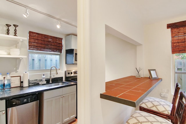 kitchen featuring rail lighting, stainless steel dishwasher, sink, white cabinets, and range