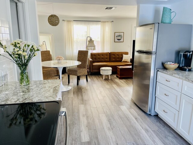 kitchen with light stone countertops, stainless steel fridge, white cabinets, and hanging light fixtures