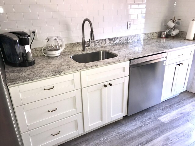 kitchen featuring white cabinets, sink, stainless steel dishwasher, decorative backsplash, and wood-type flooring