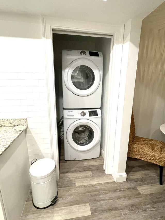 laundry room with stacked washer / drying machine, wood-type flooring, and tile walls