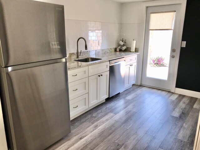 kitchen with sink, light hardwood / wood-style flooring, light stone countertops, appliances with stainless steel finishes, and white cabinetry