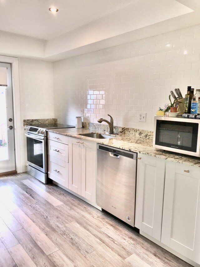 kitchen with white cabinets, sink, appliances with stainless steel finishes, and light hardwood / wood-style flooring