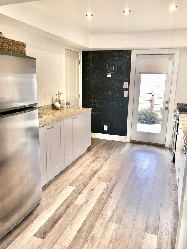 kitchen featuring white cabinets, appliances with stainless steel finishes, light hardwood / wood-style floors, and light stone counters