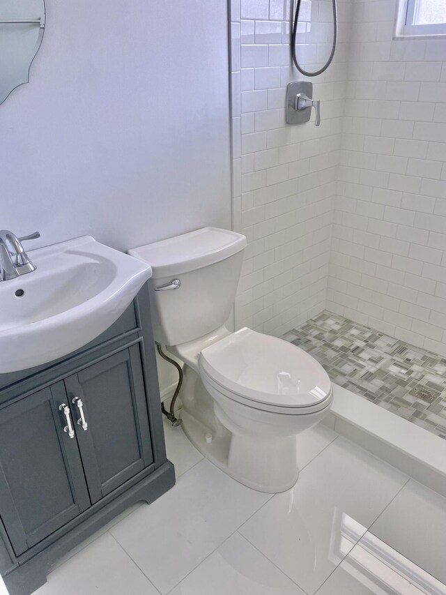 bathroom with a tile shower, tile patterned flooring, vanity, and toilet