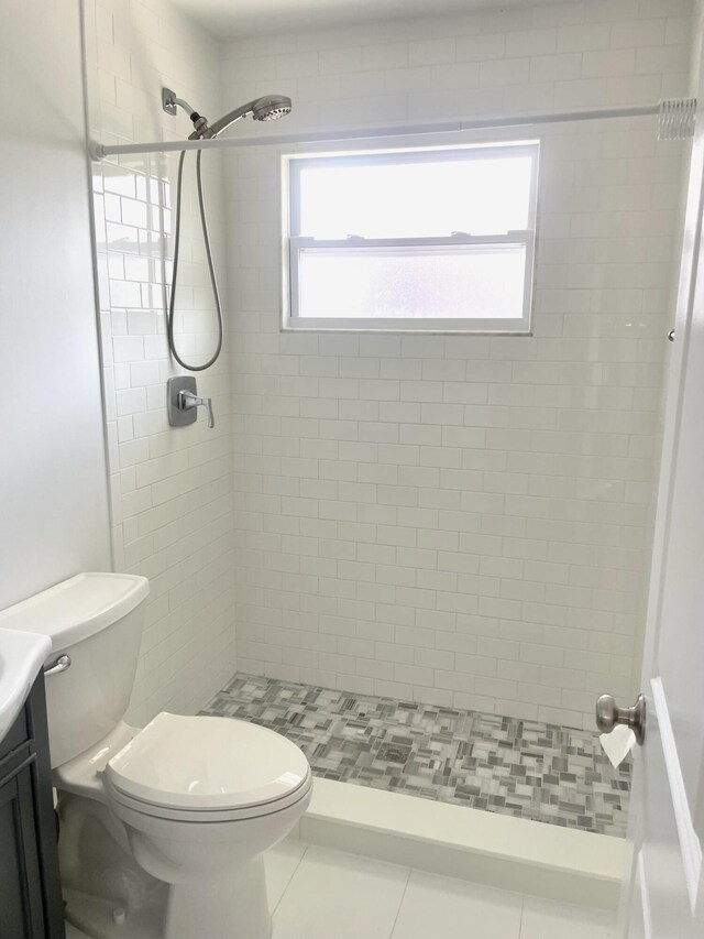 bathroom featuring toilet, a tile shower, vanity, and tile patterned floors