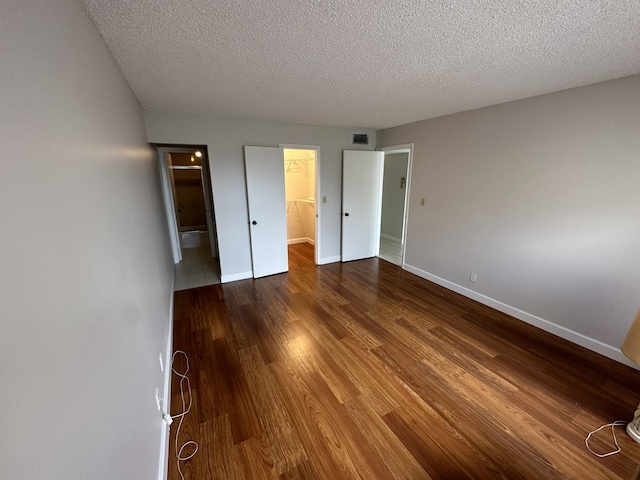 unfurnished bedroom featuring a textured ceiling, a walk in closet, a closet, and wood-type flooring